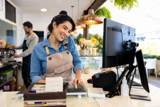 Happy waitress taking a delivery order on the phone at a coffee shop